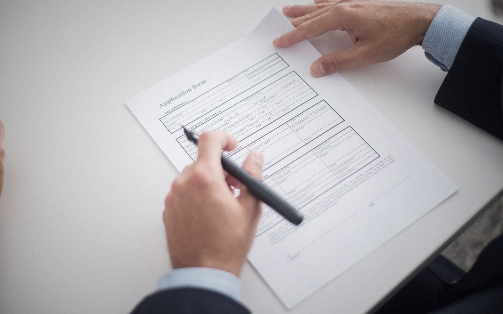 A hand holding a pen fills out a printed application form on a desk