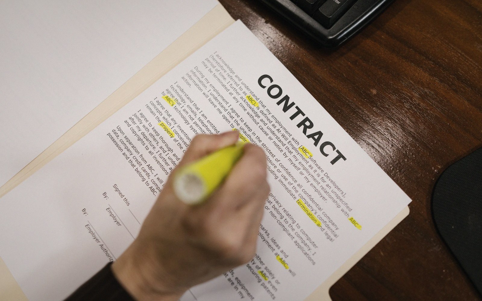 A hand highlights key terms on a printed contract with a yellow marker