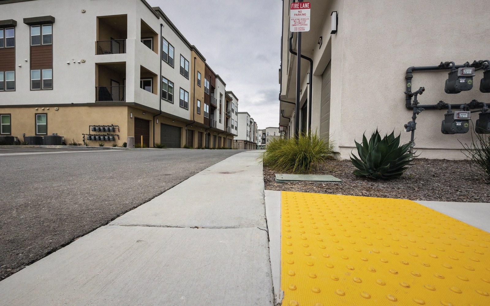 Rows of townhouses line a quiet street with a yellow tactile paving strip on the sidewalk