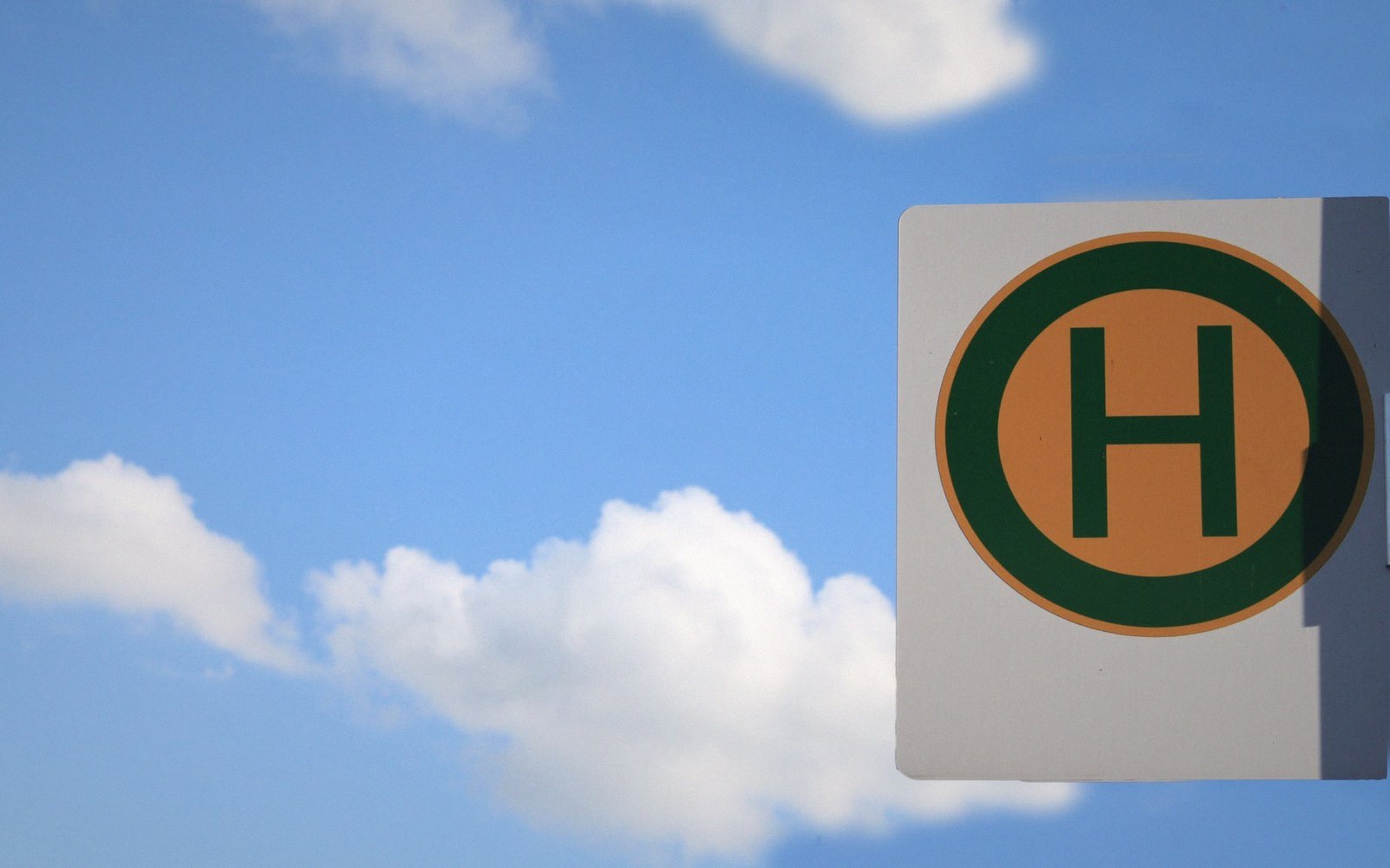 Bus stop sign with a green H in an orange circle against a blue sky