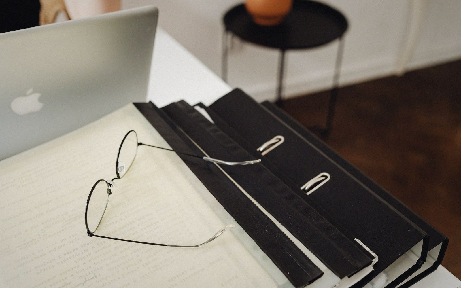 Wire-rimmed glasses resting on binders beside an open laptop on a desk