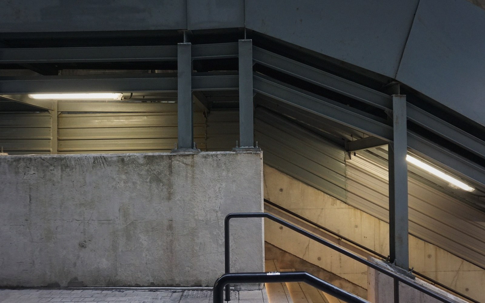 Concrete stairway with metal handrail leading down beneath a sloped structural roof