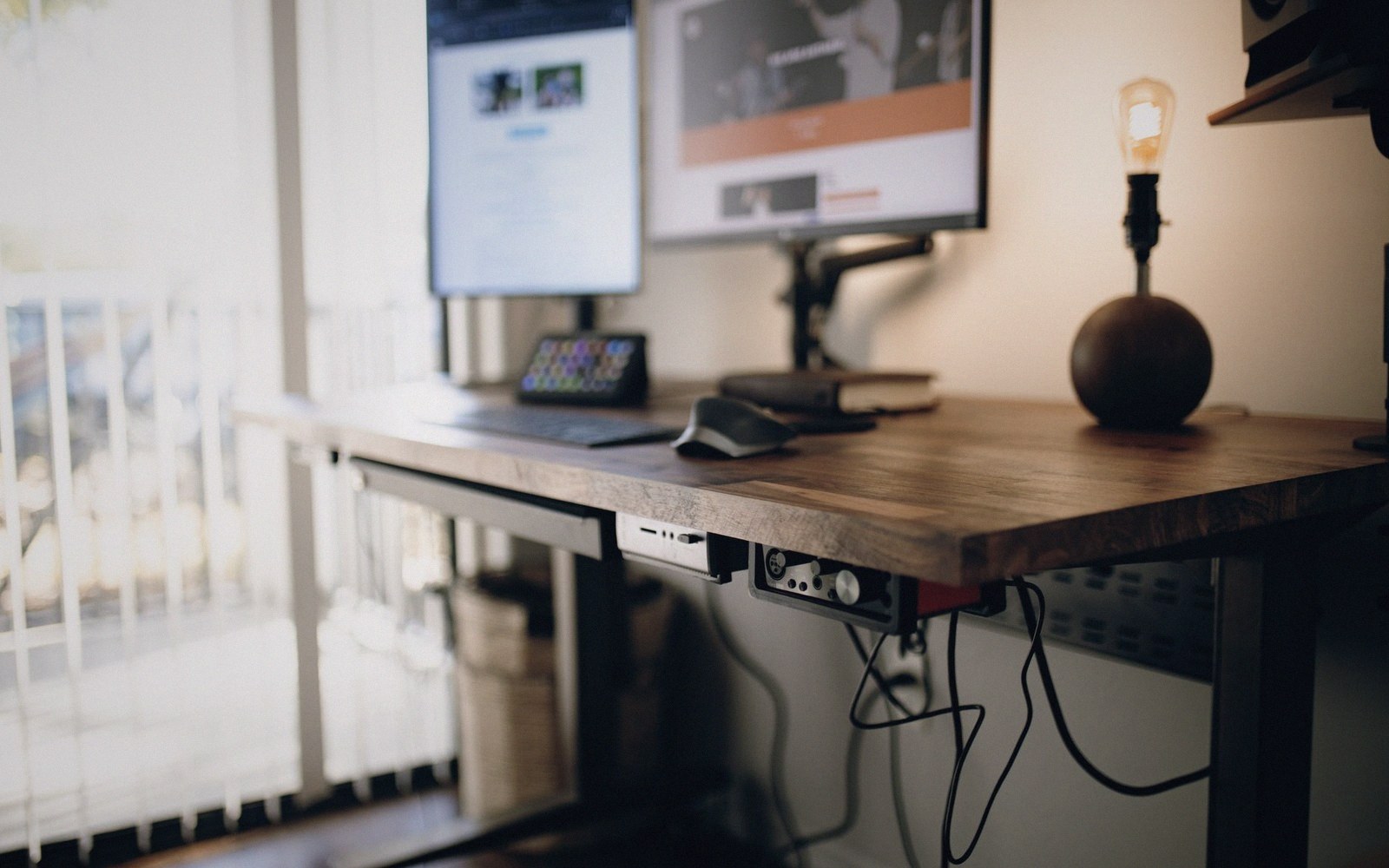 Wooden desk with dual monitors, exposed edison bulb lamp, and cable management underneath